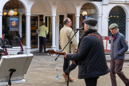 11/06/2019 Winchester, Hampshire, UK a middle aged busker signing at a microphone while playing the guitar with shoppers passing byのeditorial素材