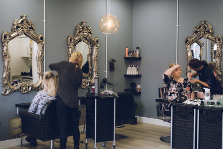 02/21/2020 Portsmouth, Hampshire, UK The interior of a hair salon with a hair dresser styling hair and a makeup artist applying makeupのeditorial素材