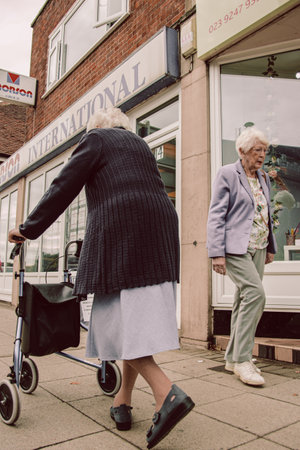 04/08/2020, Portsmouth, Hampshire, UK two elderly women walking past each other in the street, one of the women is using a zimmer frame or mobility aid to walkのeditorial素材