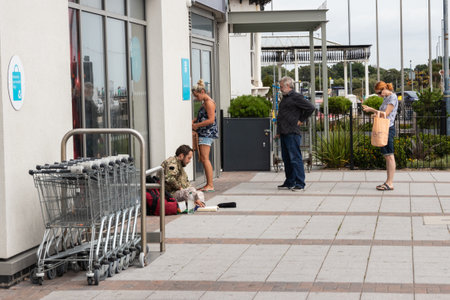 08/03/2019 Portsmouth, Hampshire, UK People queue for a cashpoint or ATM while a homeless man sits on the floor next to themのeditorial素材