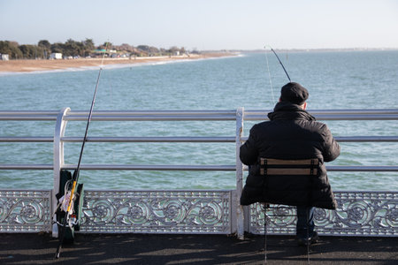 a man sitting on a pier fishing with a fishing rodの写真素材