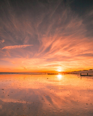a golden sunset on a sandy beach with the sun reflecting on the wet sandsの写真素材