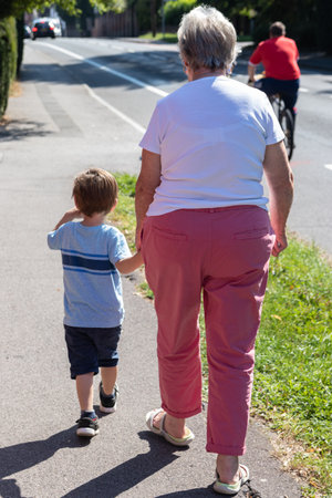 A grandmother and grandson walking down a street holding handsの写真素材