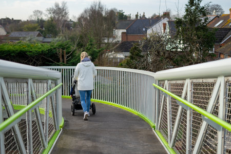 A young woman pushing a pram or pushchair over a modern metal spiral bridgeの写真素材