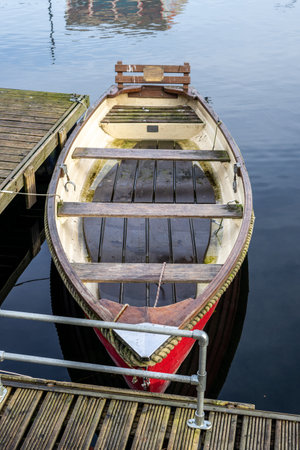 An old empty wooden rowing boat tied up on a wooden jetty on calm waterの写真素材