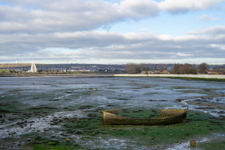 a view of tipner lake in Portsmouth, UK with an old wooden boat in the foreground at low tide also showing Brent Geese on the shoreの写真素材