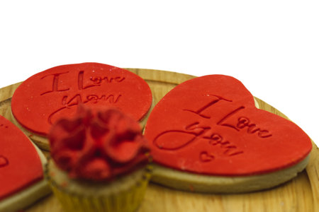 a close up of a biscuit with the words i love you on it surrounded by red cakes on a wooden chopping boardの写真素材