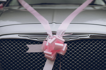 a pink wedding ribbon with a bow tied around a silver car ready to be used as a wedding carの写真素材