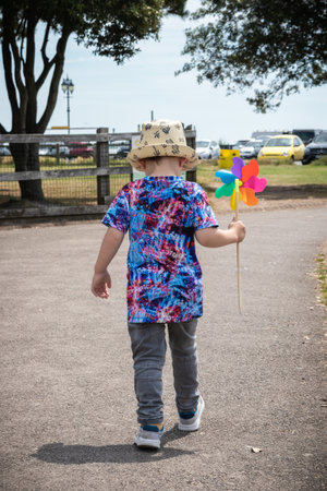 A small boy running through a park holding a multi coloured windmillの写真素材