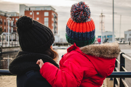 A mother holding her son in her arms looking at a view, both wearing winter clothes and a bobble hatの写真素材