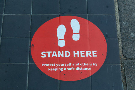 A sign on the ground outside a shop telling customers where to queue so that they are socially distance as instructed by government guidelinesの写真素材