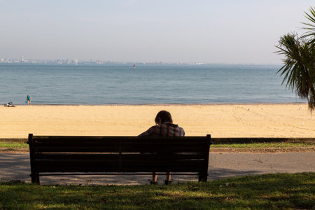 a woman sitting alone on a bench at the seaside or beachの写真素材