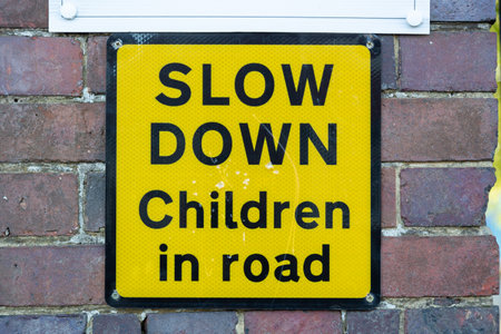 a yellow sign on a brick wall outside a school stating slow down children in roadの写真素材