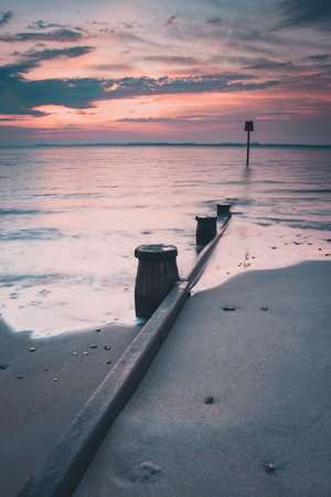 a calm sunrise at a sandy beach with a wooden beach Groyne or markerの写真素材