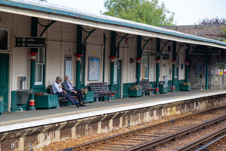 09/15/2020 Ryde, Isle of Wight, UK Two elderly men sitting on a bench on a train station platform waiting for a train to arriveのeditorial素材