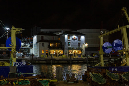 The Bridge tavern Pub in Old Portsmouth lit up at night with fishing boats in the Foregroundのeditorial素材