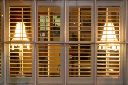 lamps in the windows of a cosy looking home though window shuttersの写真素材