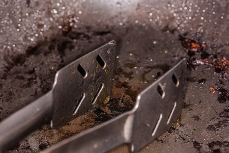 a pair of metal tongs lain in a frying pan full of fatの写真素材