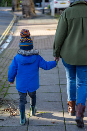 A mother and son walking together holding hands wearing winter clothingの写真素材