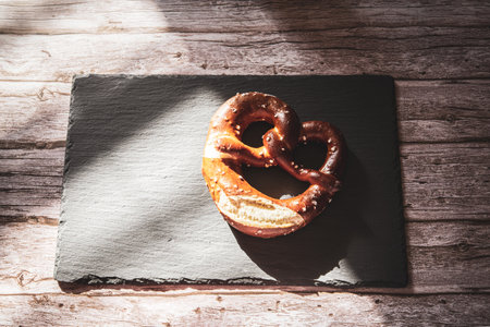 A fresh Pretzel on a slate board rested on a rustic wood tableの写真素材
