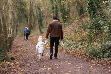 A man holding his daughters hand walking through a forest in autumnの写真素材