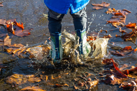 the legs of a child wearing wellies jumping in puddles splashingの写真素材