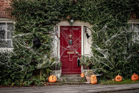 The exterior of an English countryside cottage decorated for Halloween with pumpkins on the doorstep and spiders webs or cobwebs hanging downのeditorial素材