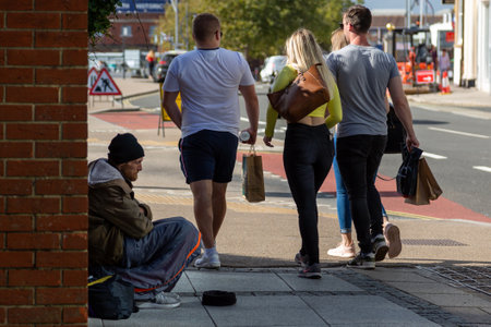 09/08/2020 Portsmouth, Hampshire, UK A group of young people walking past a homeless man begging in the streetのeditorial素材