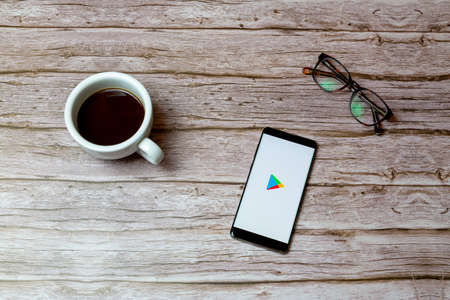 02-04-2021 Portsmouth, Hampshire, UK A Mobile phone or cell phone laid on a table or desk with the Google play store app open and a coffee next to itのeditorial素材