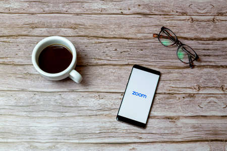 02-04-2021 Portsmouth, Hampshire, UK A Mobile phone or cell phone laid on a table or desk with the Zoom calling app open and a coffee next to itのeditorial素材