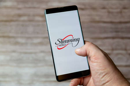02-04-2021 Portsmouth, Hampshire, UK A handing holding a Mobile phone or cell phone with the slimming world dieting app on screenのeditorial素材