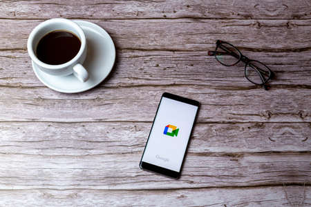 02-05-2021 Portsmouth, Hampshire, UK A mobile phone or cell phone laid on a wooden table or desk with the Google meet app openのeditorial素材