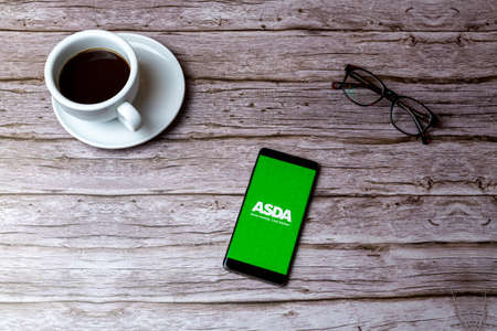 02-05-2021 Portsmouth, Hampshire, UK A mobile phone or cell phone laid on a wooden table or desk with the ASDA shopping app openのeditorial素材