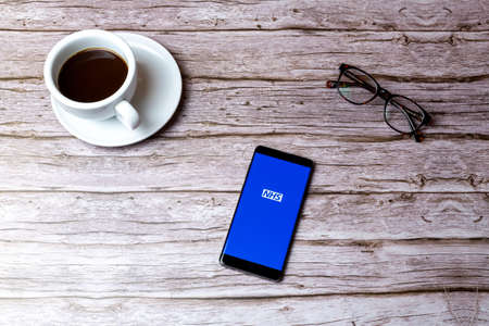 02-05-2021 Portsmouth, Hampshire, UK A mobile phone or cell phone laid on a wooden table or desk with the NHS app openのeditorial素材