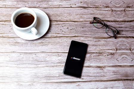02-05-2021 Portsmouth, Hampshire, UK A mobile phone or cell phone laid on a wooden table or desk with the Deezer Music app openのeditorial素材