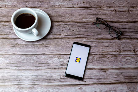 02-05-2021 Portsmouth, Hampshire, UK A mobile phone or cell phone laid on a wooden table or desk with the Lidl supermarket app openのeditorial素材