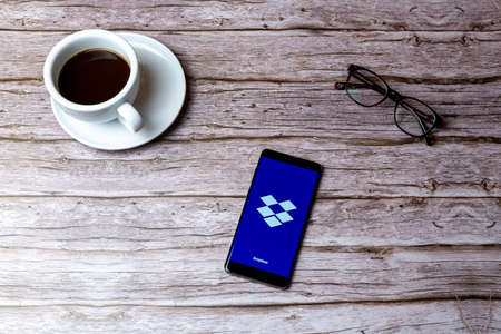 02-05-2021 Portsmouth, Hampshire, UK A mobile phone or cell phone laid on a wooden table or desk with the Dropbox app openのeditorial素材