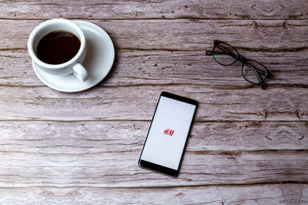 02-05-2021 Portsmouth, Hampshire, UK A mobile phone or cell phone laid on a wooden table or desk with the H&M app openのeditorial素材