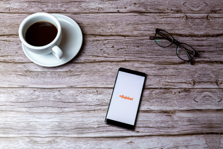 02-05-2021 Portsmouth, Hampshire, UK A mobile phone or cell phone laid on a wooden table or desk with the Babbel language app openのeditorial素材