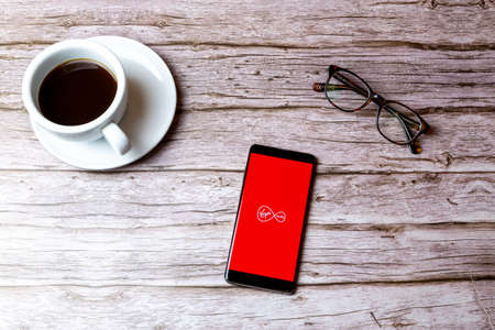02-08-2021 Portsmouth, Hampshire, UK A mobile phone or cell phone laid on a wooden table with the Virgin media app open next to a coffee and glassesのeditorial素材