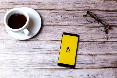 02-08-2021 Portsmouth, Hampshire, UK A mobile phone or cell phone laid on a wooden table with the app yellow pages open next to a coffee and glassesのeditorial素材