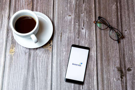 02/10/2021 Portsmouth, Hampshire, UK A mobile phone or cell phone laid on a wooden table with the British Gas app open on screen next to a coffeeのeditorial素材