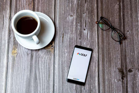 02/10/2021 Portsmouth, Hampshire, UK A mobile phone or cell phone laid on a wooden table with the Golf Channel app open on screen next to a coffeeのeditorial素材
