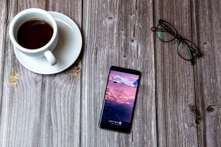 02/10/2021 Portsmouth, Hampshire, UK A mobile phone or cell phone laid on a wooden table with the United airlines app open on screen next to a coffeeのeditorial素材