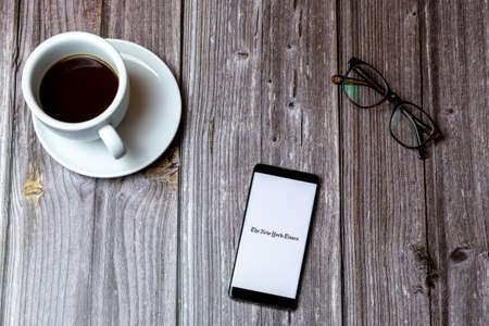 02/10/2021 Portsmouth, Hampshire, UK A mobile phone or cell phone laid on a wooden table with the New York Times app app open on screenのeditorial素材