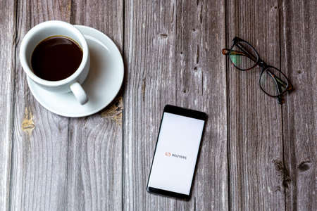 02/10/2021 Portsmouth, Hampshire, UK A mobile phone or cell phone laid on a wooden table with the Reuters News app open on screen next to a coffeeのeditorial素材