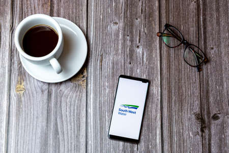 02/10/2021 Portsmouth, Hampshire, UK A mobile phone or cell phone laid on a wooden table with the South west water app open on screen next to a coffeeのeditorial素材