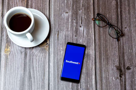 02/10/2021 Portsmouth, Hampshire, UK A mobile phone or cell phone laid on a wooden table with the Southwest airline app open on screen next to a coffeeのeditorial素材