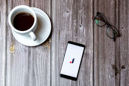 02/10/2021 Portsmouth, Hampshire, UK A mobile phone or cell phone laid on a wooden table with the joom app open on screen next to a coffeeのeditorial素材