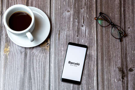 02/10/2021 Portsmouth, Hampshire, UK A mobile phone or cell phone laid on a wooden table with the barcelo Hotels app open on screen next to a coffeeのeditorial素材